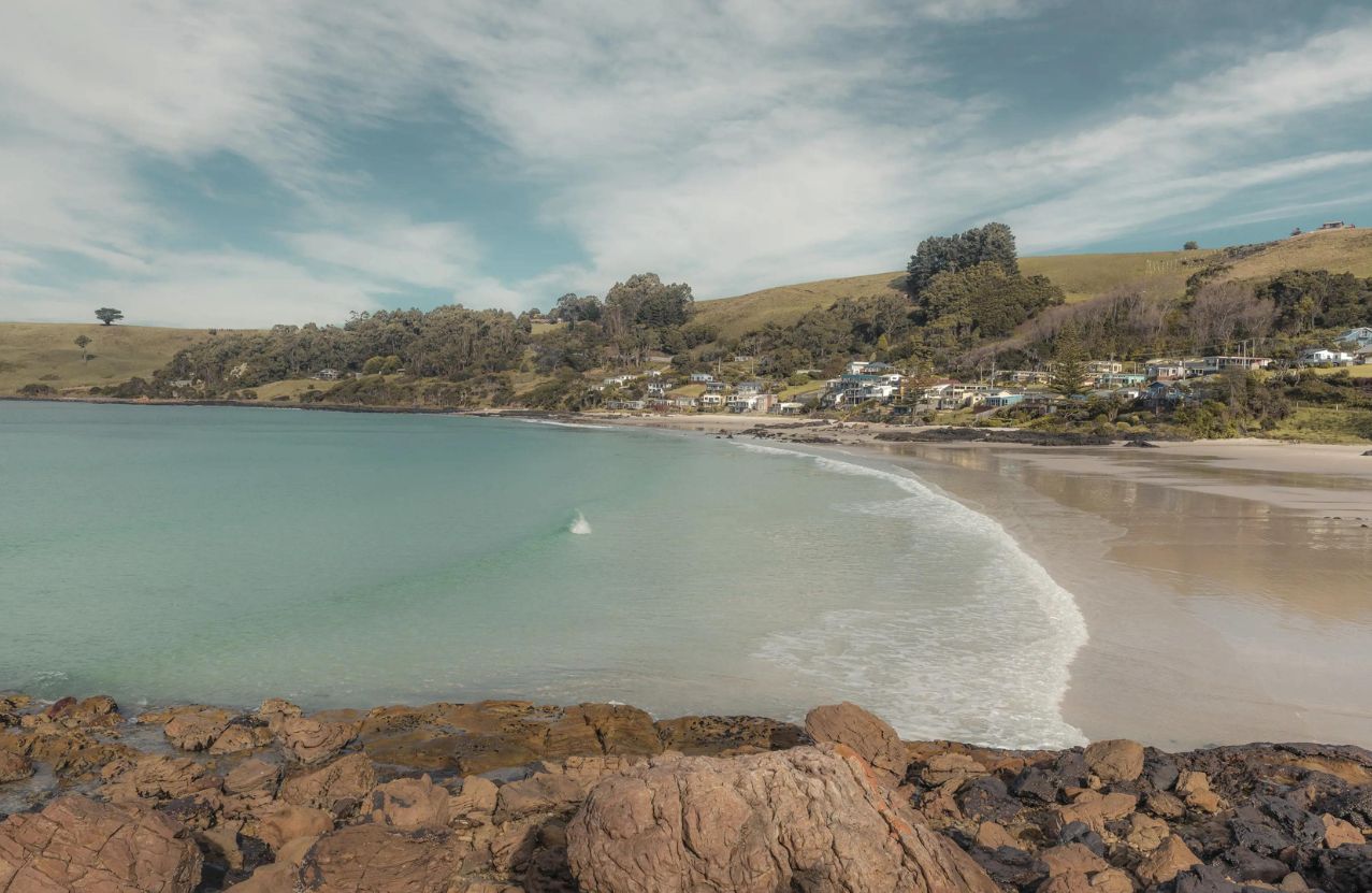 Boat Harbour, a calm bay, a village on the hill, and rocks in the foreground.