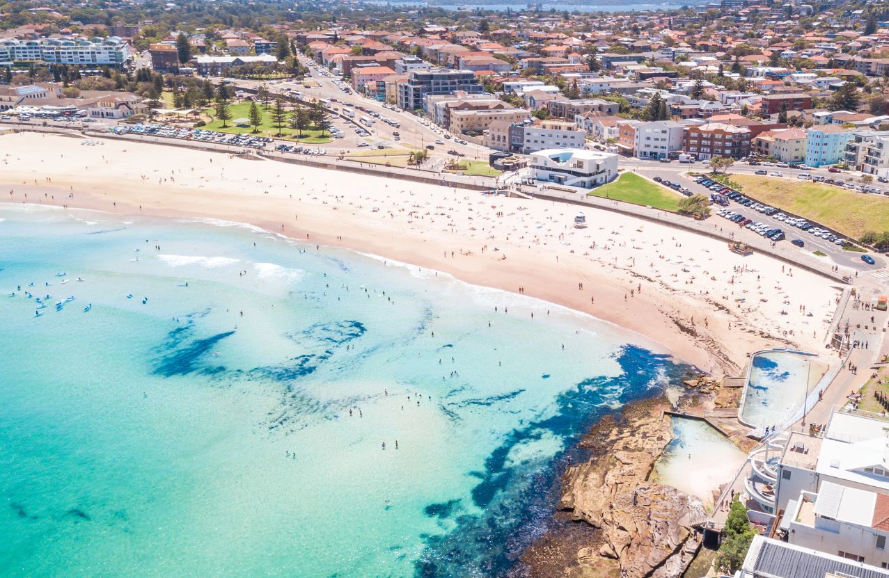 Aerial view of Bondi Beach, the curve of sand packed with swimmers and the suburb behind the promenade.