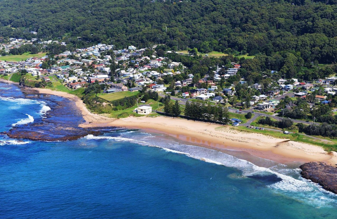 Coledale from the air, the village tucked into forest above a short sandy beach.
