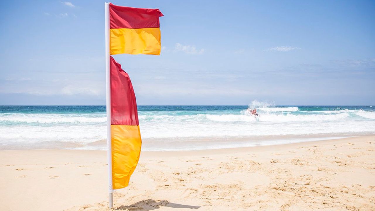 Red and yellow surf lifesaving flags on a patrolled Australian beach, with a swimmer in the break behind them.