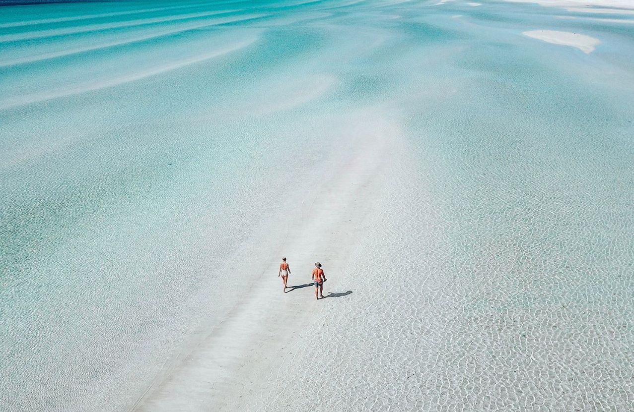 Flaherty’s Beach, two people walking a sandbar through ankle-deep clear water.