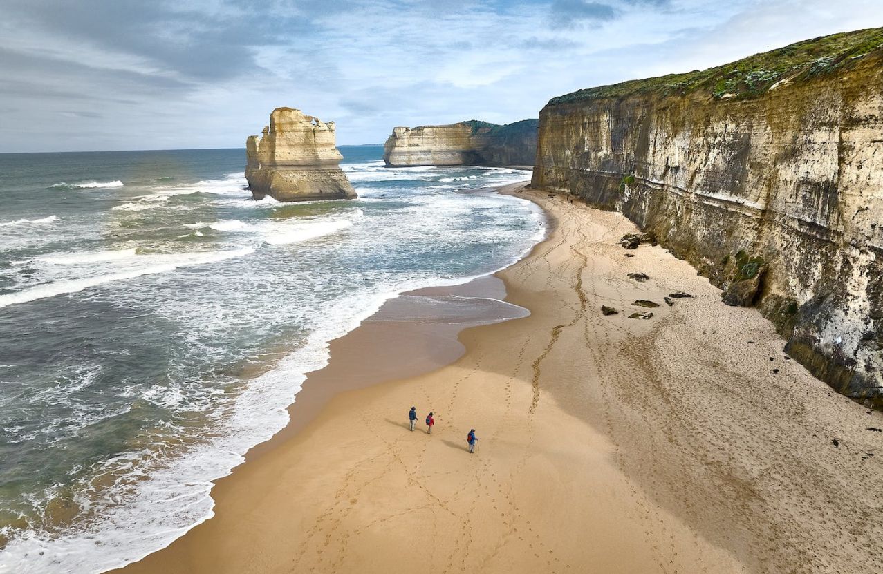 Gibson Steps, three walkers on the sand beneath the Twelve Apostles and the cliff.