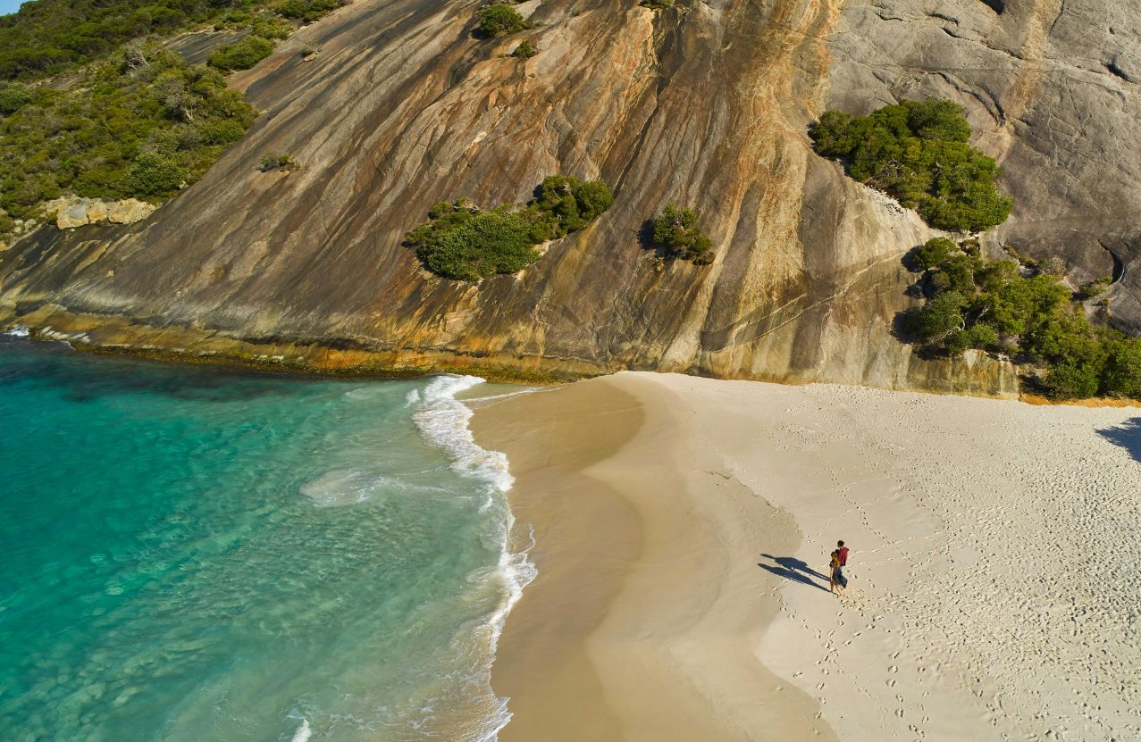 Misery Beach, two people on a small apron of sand under a vast granite wall.