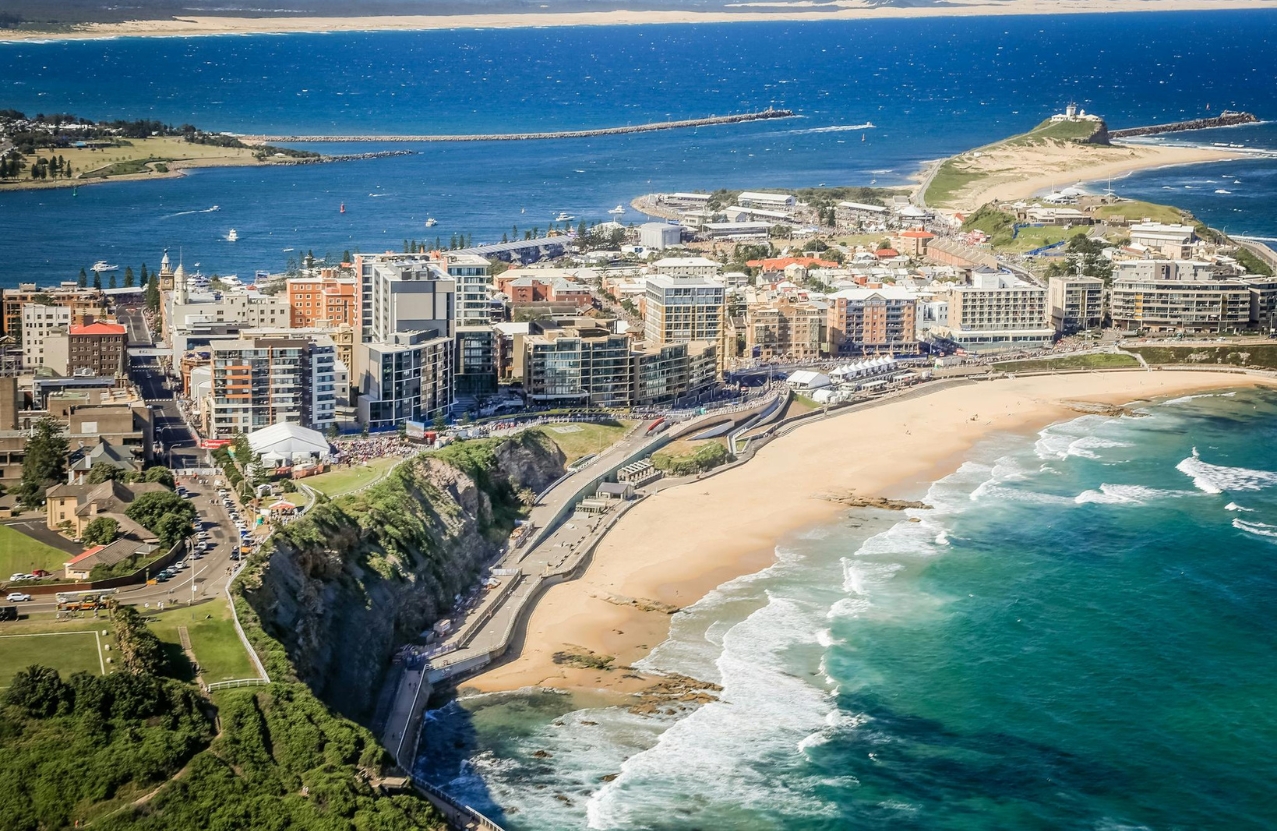 Aerial of Newcastle Beach, the city on the cliff and Nobby’s headland across the bay.
