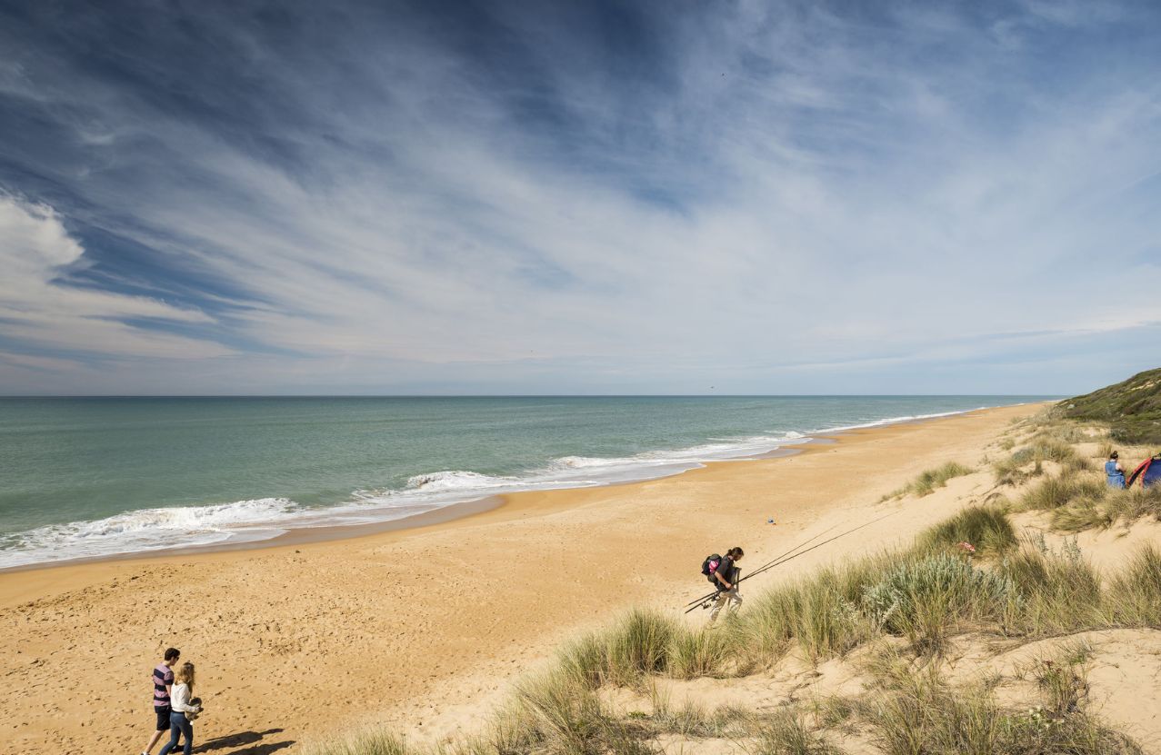 Ninety Mile Beach, fishers on the dune and a long empty shore under streaked cloud.