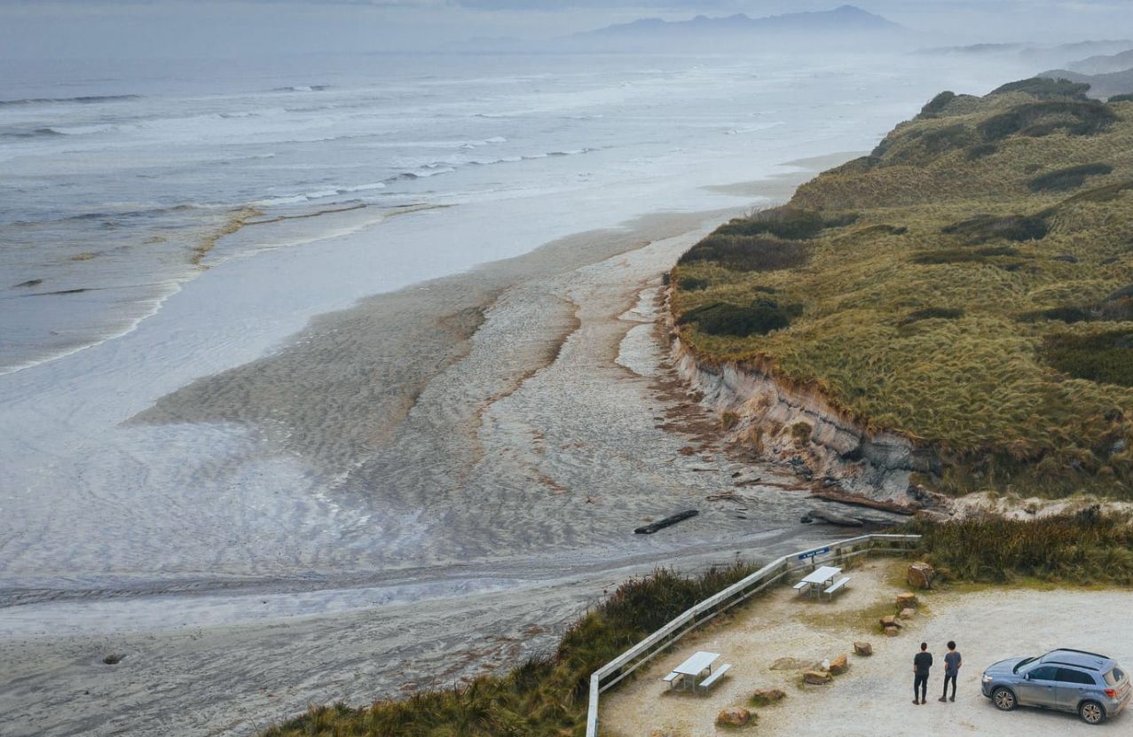 Ocean Beach near Strahan, wind-cut sand, dune grass, and a grey Southern Ocean.