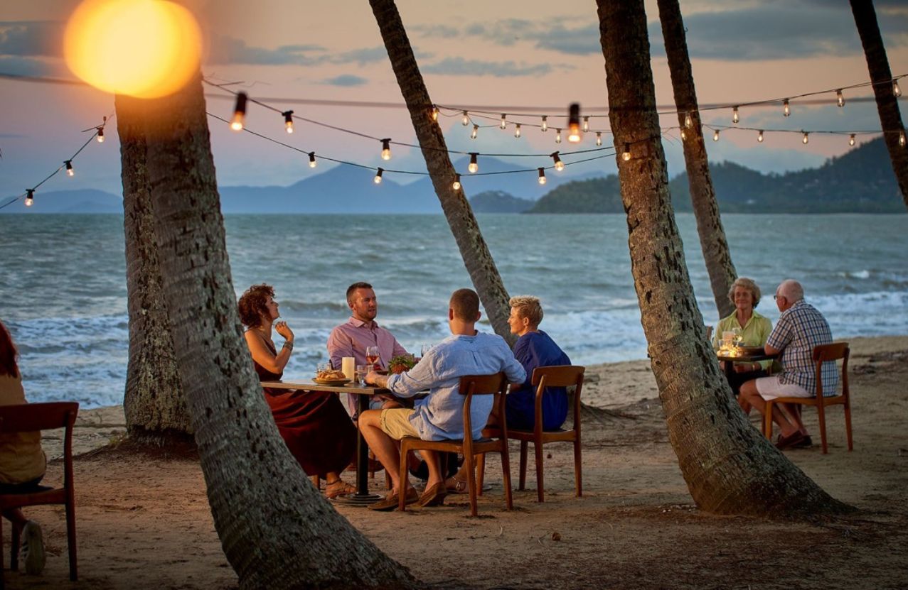 Dinner under the palms at Palm Cove, festoon lights and the Coral Sea at dusk.