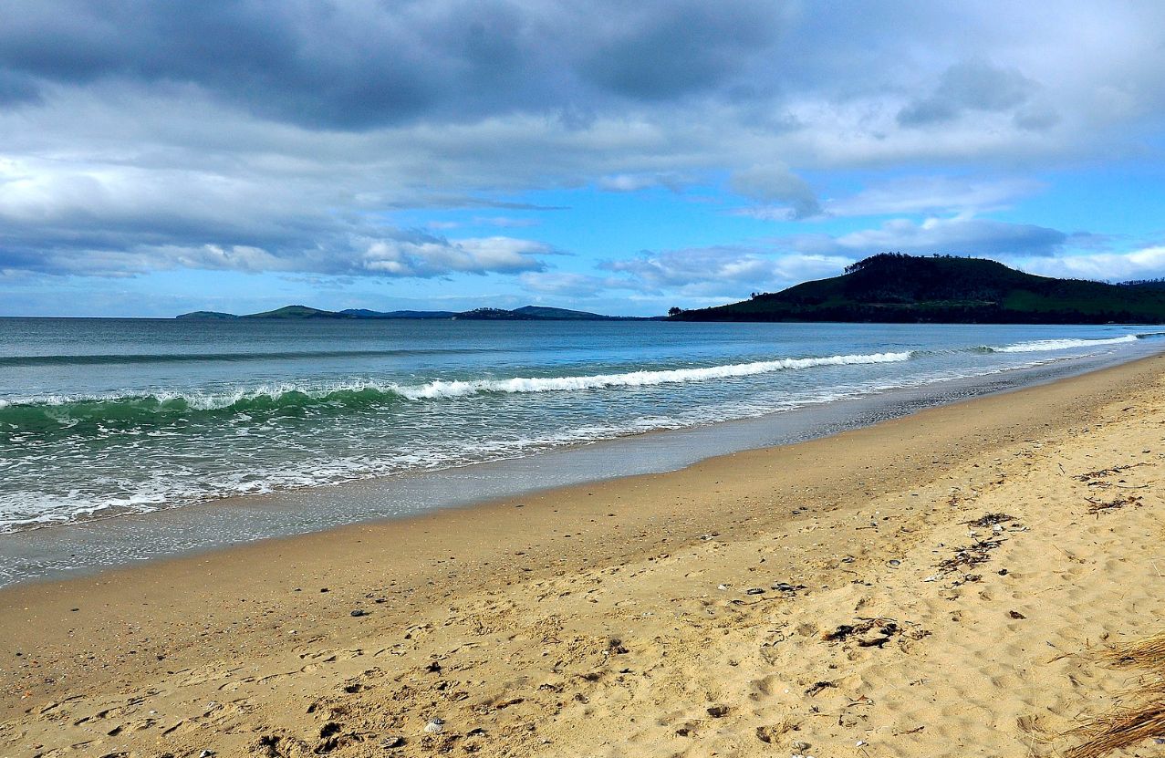 Seven Mile Beach under a broken sky, a long straight shore and a green headland.
