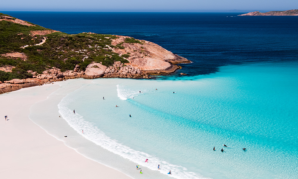 An Esperance curve of white sand, swimmers in luminous water off a granite point.